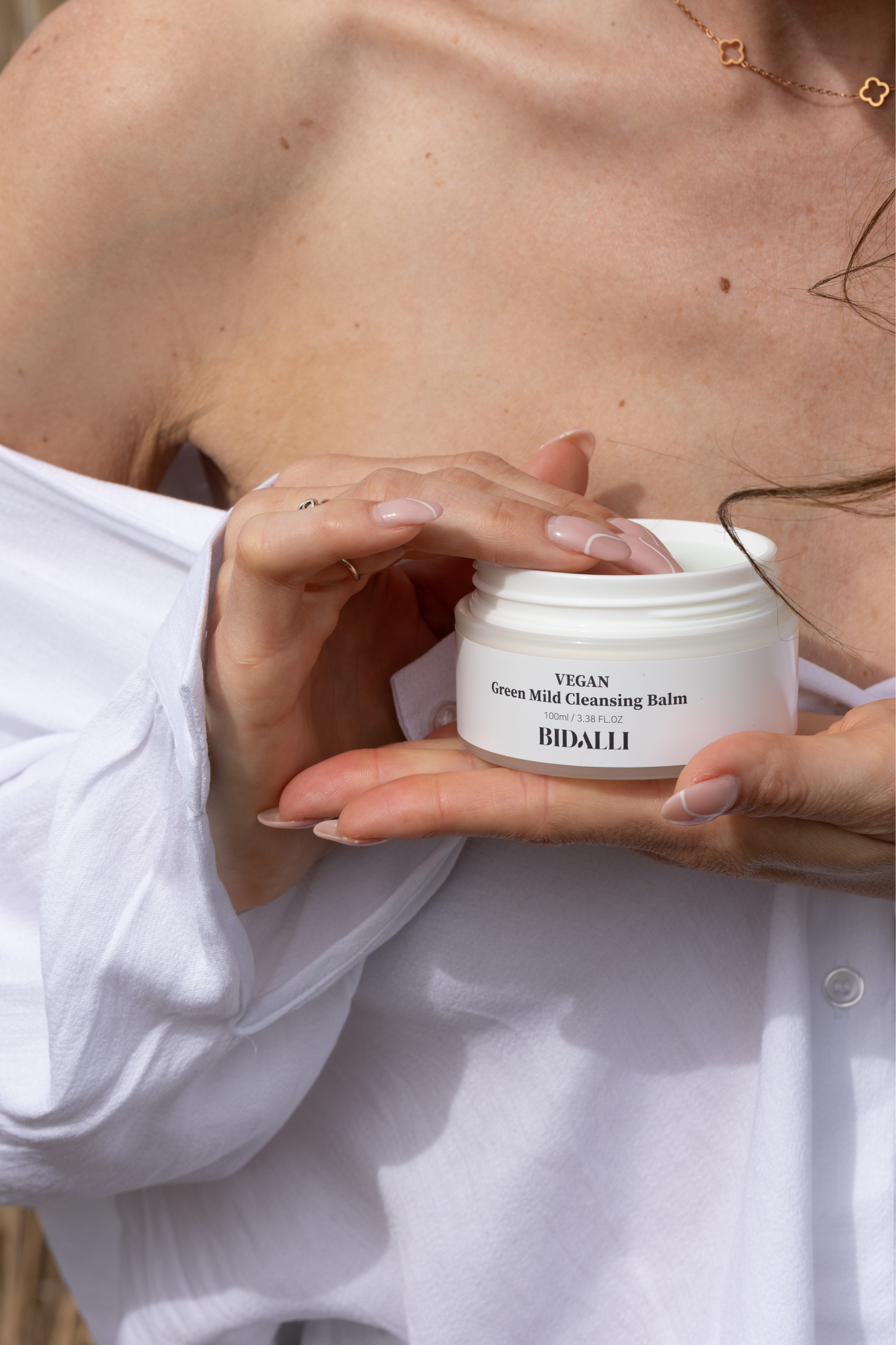 Close up of a woman's hands with her fingers in a jar of Bidalli's Green Mild Cleansing Balm. Available for purchase at Sinless Skincare.