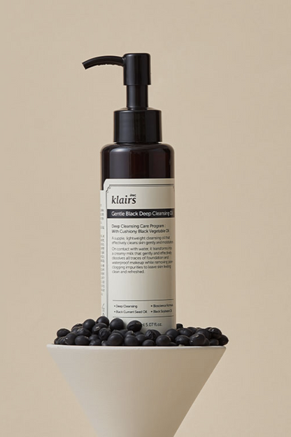 Klairs' Gentle Black Deep Cleansing Oil sitting on a beige bowl filled with black colored berries, against a beige background.