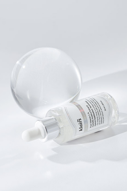 Bottle of Klairs' Freshly Juiced Vitamin Drop lying on its side in front of a glass sphere, against a light grey background.