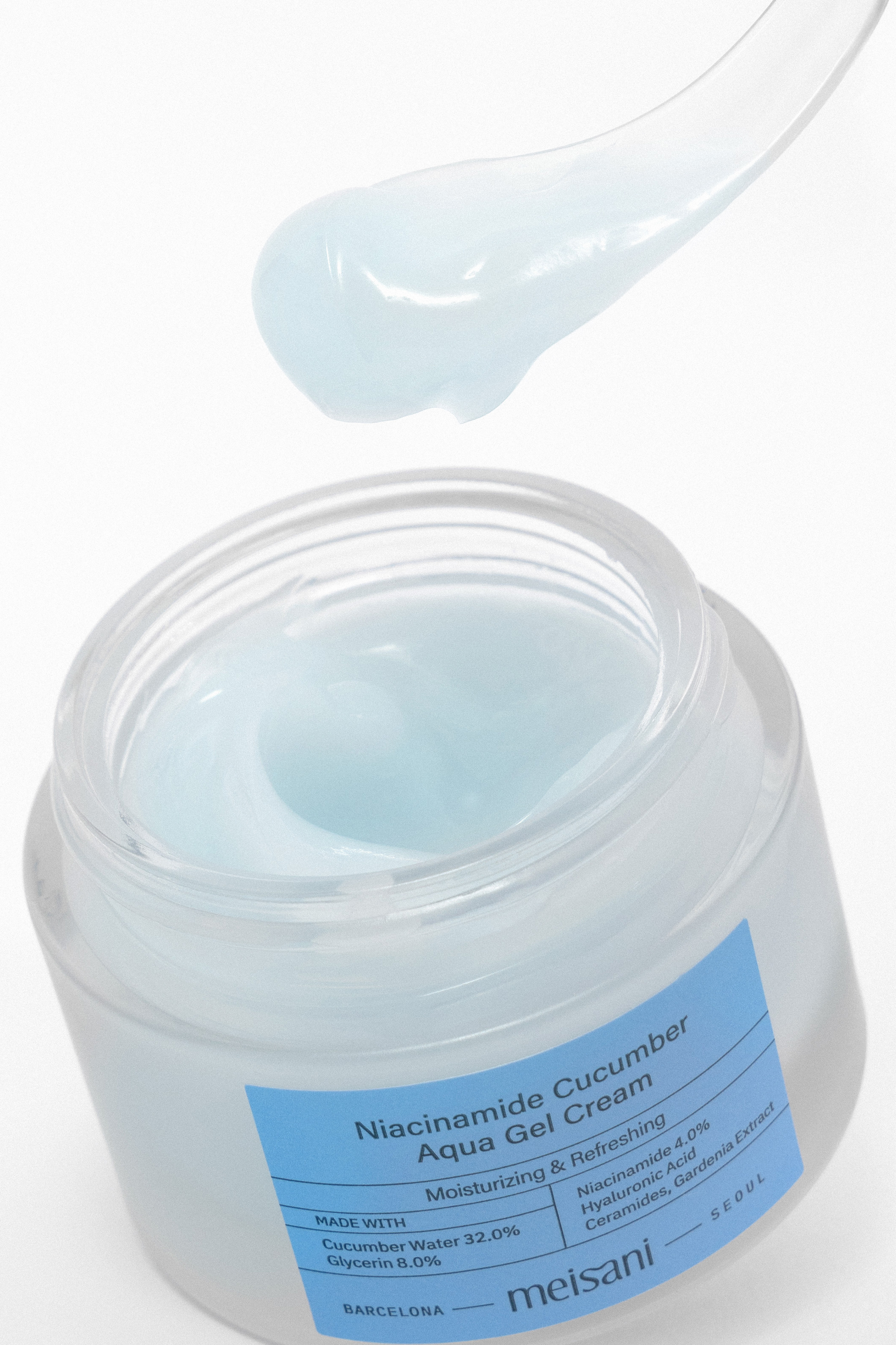 An open jar of Meisani's Niacinamide Cucumber Aqua Gel Cream against a white background. A spatula with cream on it is above the jar.