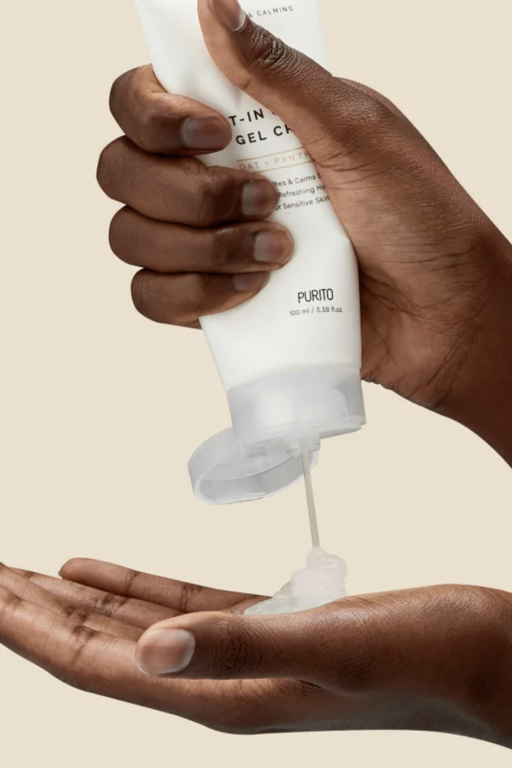 A woman is squeezing Purito's Oat-in Gel Calming Cream onto her hand. Her hands are seen against a beige background. Available for purchase at Sinless Skincare.