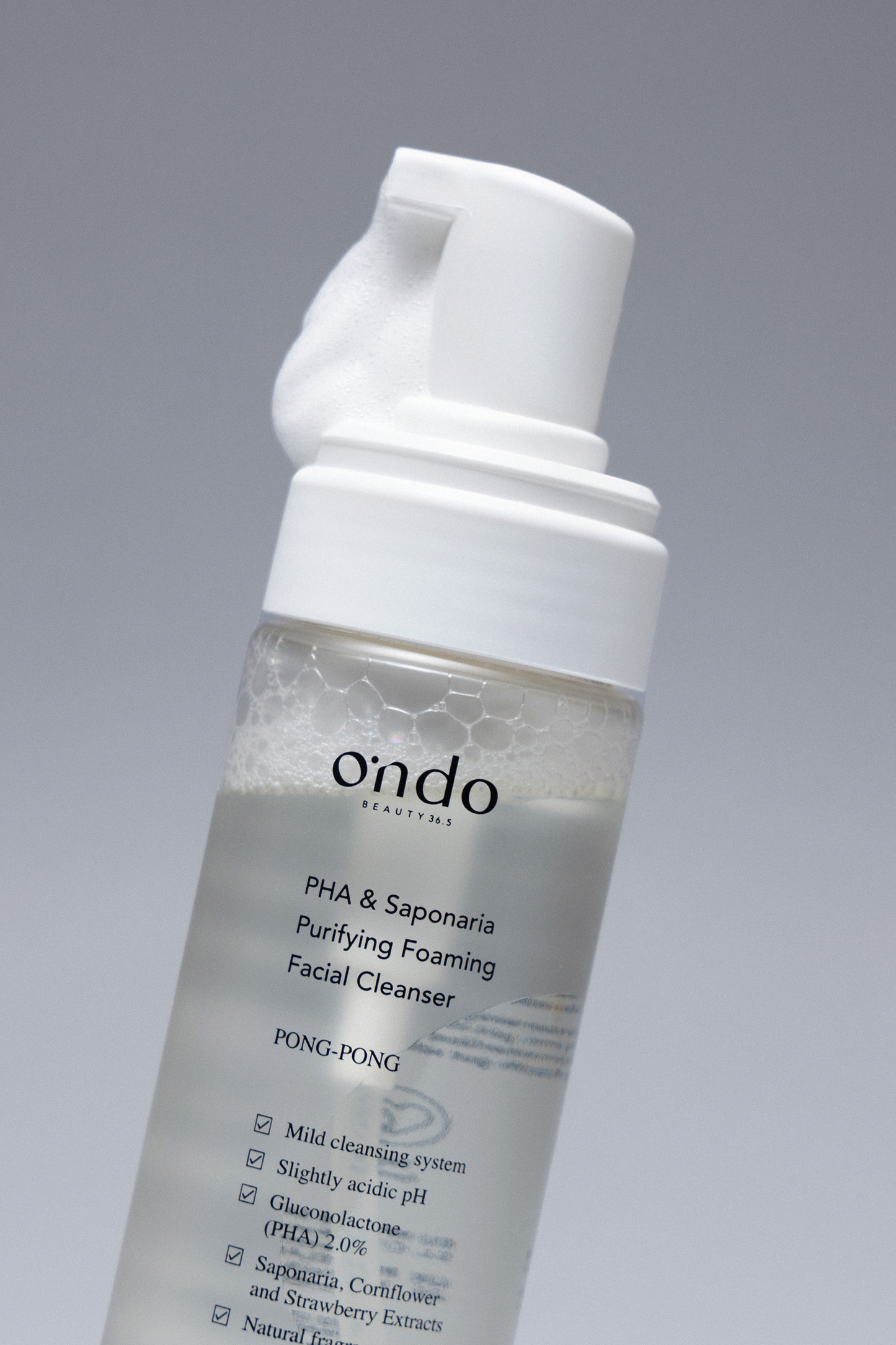 Close up of Ondo Beauty 36.5 PHA & Saponaria Foaming Cleanser with foam coming out from the top, against a grey background. Available for purchase at Sinless Skincare.