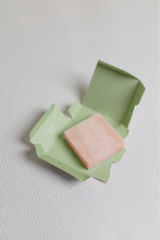 Load image into Gallery viewer, Pink Bar of Ondo Beauty 36.5&#39;s Calamine &amp; Oatmeal Cleansing Bar laying on its light green unfolded box, against a textured light grey background.
