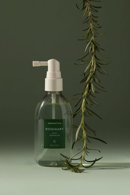 Bottle of Aromatica's Rosemary Root Enhancer against a soft green background, with a twig of Rosemary hanging down next to it.