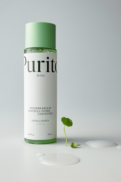 Purito's Wonder Releaf Centella Toner Unscented standing against a light grey background. There are two puddles of toner on ground and a piece of centella plant. Available at Sinless Skincare.