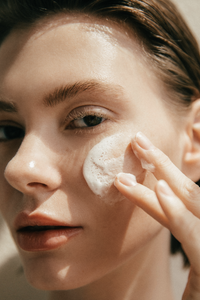 Close up of woman applying Aromatica's Tea Tree Balancing Cleanser to her cheek.