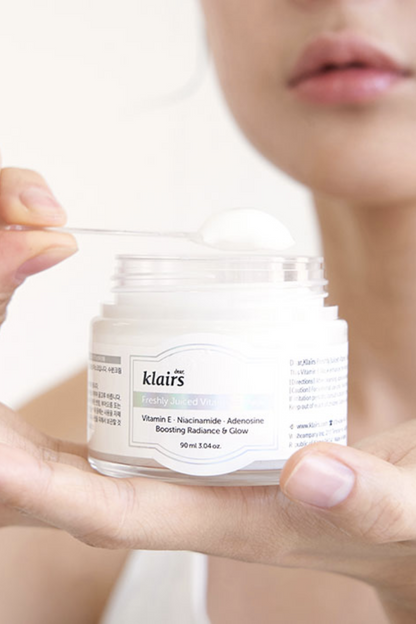 Close up of woman's hand with a jar of Klairs' Freshly Juiced Vitamin E Mask resting on top. Her other hand is holding a spatula with cream on it.