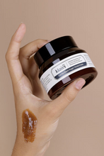 Lade das Bild in den Galerie-Viewer, Close up of woman&#39;s hand holding up a jar of Klairs Gentle Black Sugar Facial Polish against a beige background. There is a brown smear of exfoliator on the side of her hand.
