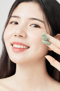 Close up of smiling woman holding up two fingers that have been dipped in Licorne's Matcha Wash Off Pack.