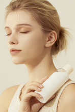 Lade das Bild in den Galerie-Viewer, A blond woman with closed eyes is holding a bottle of Purito&#39;s Oat-in Silky Toner against her shoulder. Available for purchase at Sinless Skincare.
