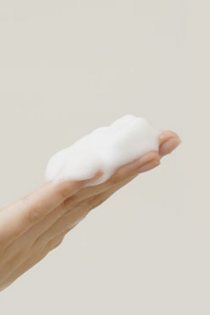 Texture shot of Klairs' Rich Moist Foaming Cleanser bubbles on a person's hand, against a light grey background.