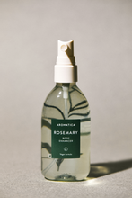 Load image into Gallery viewer, Front view of Aromatica&#39;s Rosemary Root Enhancer against a soft grey background, with a twig of Rosemary magnified from behind the transparent bottle.
