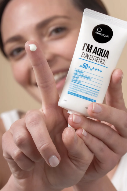 Close-up of a woman holding a tube of Suntique's I'm Aqua Sun Essence sunscreen in one hand, with a dot of the product displayed on the index finger of her other hand.