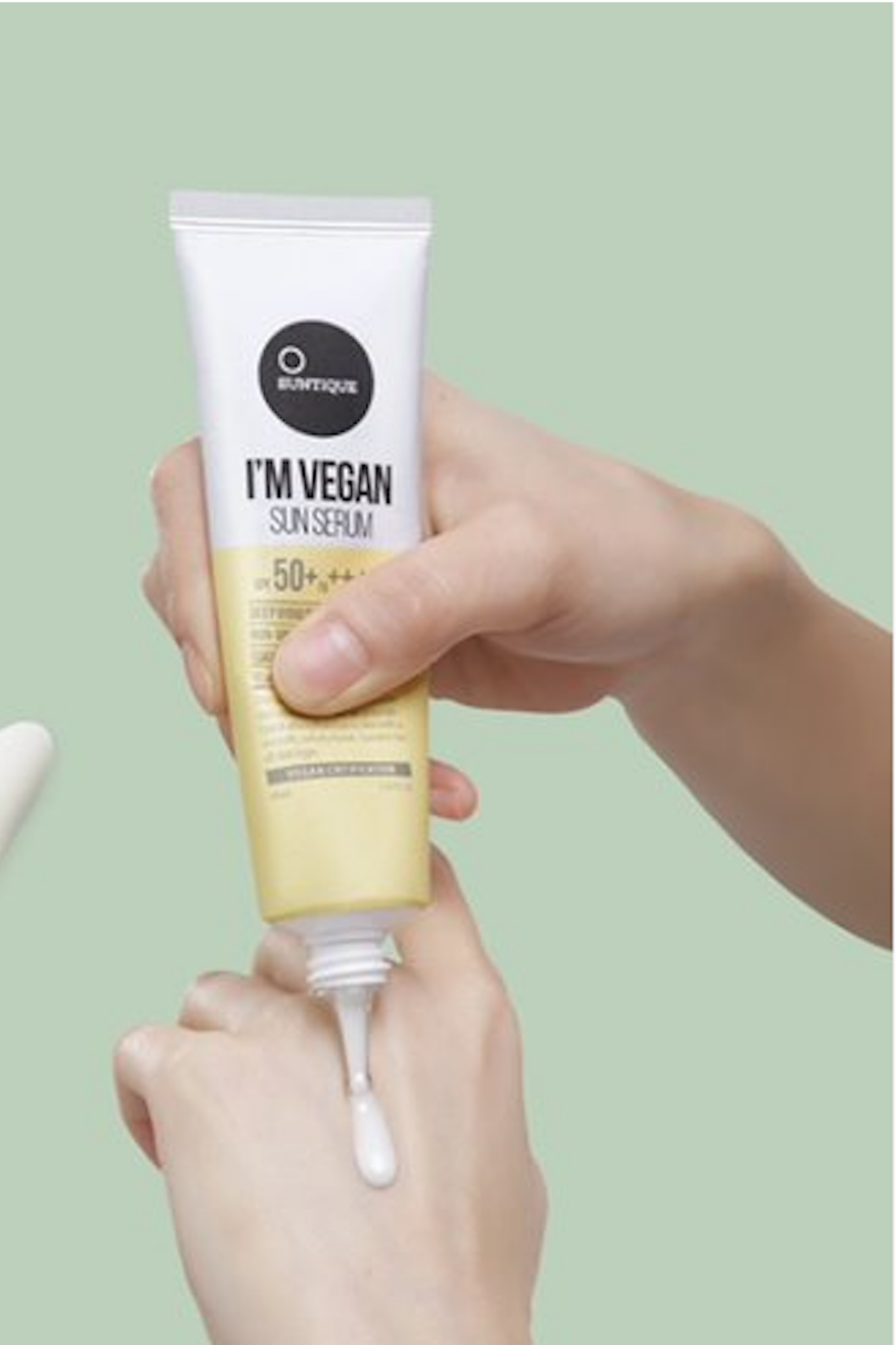 Close up of sunscreen being squeezed out of tube onto woman's hand against a light green background. Suntique I'm Vegan Sun Serum SPF